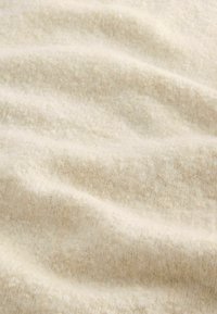 Tissu en polaire de couleur écrue avec une surface douce et texturée, présentant des variations subtiles d'épaisseur et un aspect légèrement duveteux.