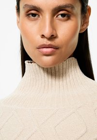 Maglione a collo alto beige a coste con un motivo a diamante testurizzato, caratterizzato da un collo alto e una finitura liscia.