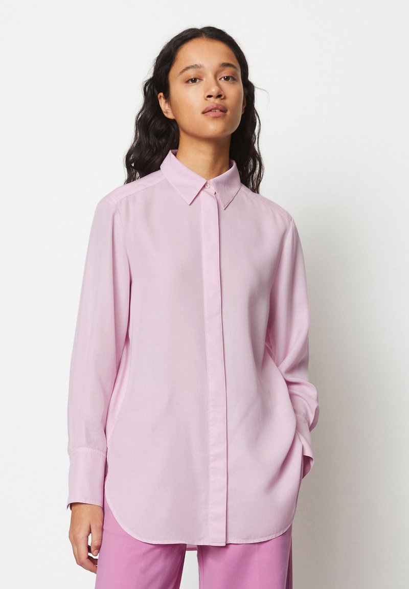 Camicia a maniche lunghe rosa chiaro con colletto abbottonato, taglio dritto e spacchi laterali, realizzata in un tessuto morbido. Abbinata a pantaloni rosa.