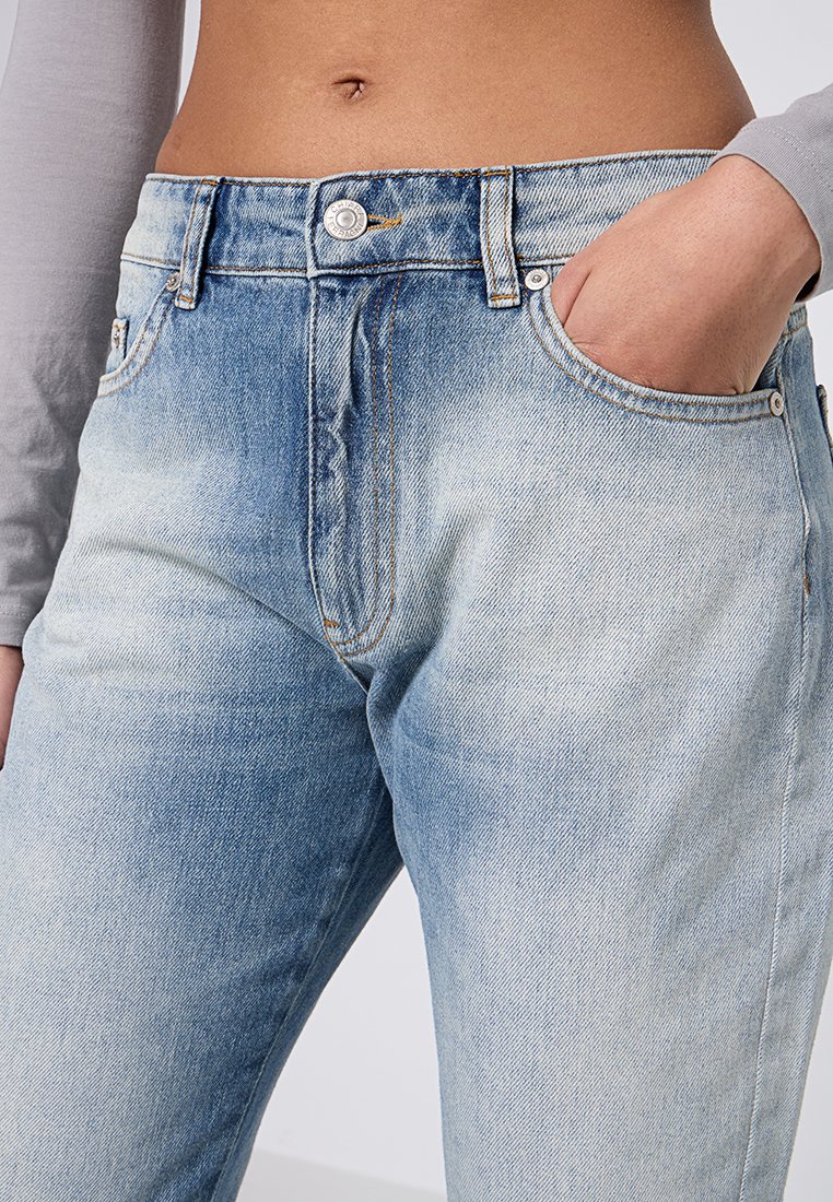 Jeans de mezclilla de color azul claro con textura deslavada, cintura de altura media, cinco bolsillos y un cierre de botón plateado con costuras en contraste.