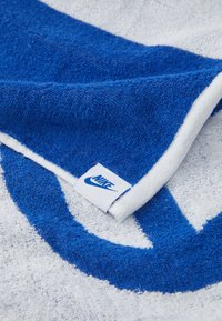 Toalha azul e branca com textura felpuda, apresentando um grande logótipo da Nike em azul e um rótulo branco com o logótipo da Nike costurado na borda.