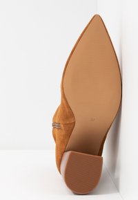Zapato de ante marrón con punta afilada, tacón bajo y soleado texturizado. Tamaño 37 marcado en la parte inferior. Diseño sencillo, sin adornos adicionales.