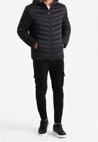 Sort polstret jakke med hætte, med en frontlynlås og vandrette syninger. Bæres med sorte cargo-bukser og sorte sneakers.