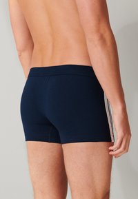 Boxer shorts in cotone elasticizzato blu navy con un design aderente, caratterizzati da strisce laterali di colore chiaro. La cintura è elastica per garantire comfort.