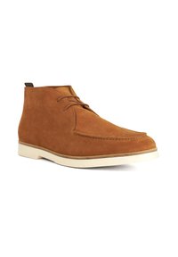 Tan suede chukka boot with a smooth finish, white rubber sole, and simple lace-up design. Features subtle stitching and a short ankle height.