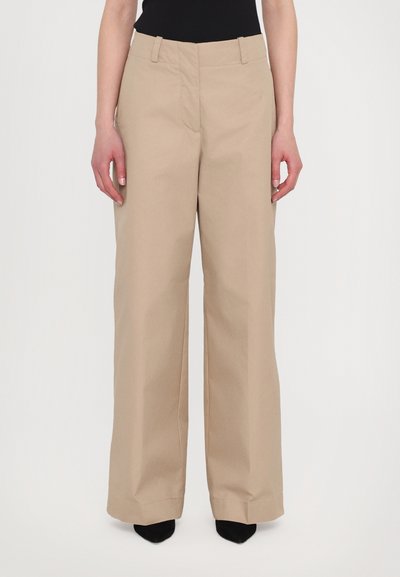 Beige wide-leg trousers with a flat front, belt loops, and a smooth texture, paired with black high-heeled shoes.