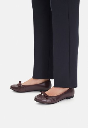 Brązowe baleriny z miękkiej skóry z pikowanym wzorem, ozdobione kokardką i perłowym akcentem na palcach, zestawione z granatowymi, dopasowanymi spodniami.