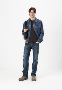 Denim jacket, black t-shirt, blue jeans, and beige footwear. Model holds a black crossbody bag. Simple, casual outfit with contrasting colors.