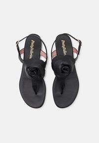 Svarta platta sandaler med blomsterdetalj i svart tyg på tådelen, minimalistisk design och en rem runt ankeln bak. Mjukt innerfoder i rosa.