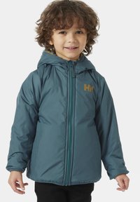 Giacca a vento teal con chiusura a cerniera, cappuccio regolabile e logo marrone sul petto. Presenta una texture liscia e foderato caldo.