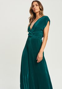Robe maxi plissée en sarcelle avec un décolleté en V profond, des manches courtes et une taille cintrée, tissu fluide et éclat subtil.