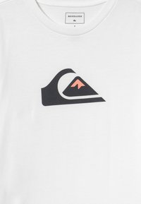 Fehér pamut póló, fekete hegy és hullám grafikával, rózsaszín kiegészítővel. A címke felirata: "Quiksilver". Klasszikus kerek nyakkivágás.