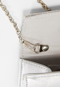 Bolso de mano metálico plateado con cadena y cierre de cremallera, que presenta una textura suave y un interior forrado de tela.
