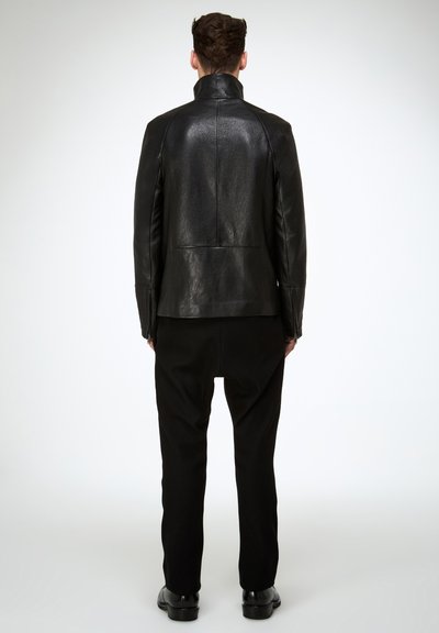 Schwarze Lederjacke mit hohem Kragen, glatter Textur und maßgeschneiderter Passform, kombiniert mit schwarzer Hose und polierten Schuhen.