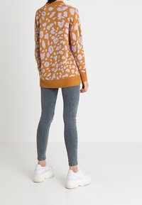 Stickad senapsgul tröja med lavendelfärgad leopardtryck, ribbade muddarna och fållen, kombinerad med grå smala jeans och vita sneakers.