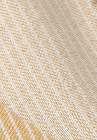 Gros plan sur un tissu tissé beige et blanc avec un motif diagonal et une texture subtile visible à la surface.