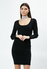 Schwarzes Bodycon-Kleid mit langen Ärmeln, das über eine gerippte Struktur und das Muster "INFLUENCER" verfügt. Glattes Material und ein runder Ausschnitt. Silbernes Choker-Accessoire.