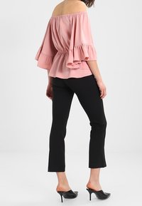 Blouse décolletée en tissu rose clair avec des manches volantes, associée à un pantalon noir cropped et des mules noires à bout ouvert.