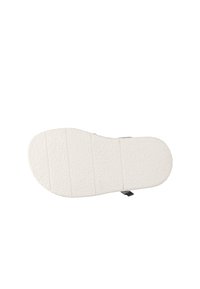 Bílá guma obuvi s texturovaným povrchem a horizontálními drážkami pro trakci, s křivkovitým tvarem a bočním štítkem.