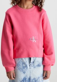 Felpa di cotone rosa con collo rotondo, polsini a costine e vestibilità corta. Presenta un logo ricamato bianco sul davanti.