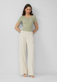 Jasnozielona prążkowana bluzka z krótkim rękawem, z dekoltem w serek i frontowymi guzikami, zestawiona z szerokimi kremowymi spodniami cargo z bocznymi kieszeniami.