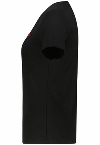 Sort kortærmet t-shirt vist fra siden med et lille rødt mærke nær brystområdet på en hvid baggrund.