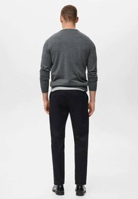 Grå stickad tröja med rund halsringning, i kombination med mörka byxor och svarta skor. Synlig sömnad på ärmar och midja.