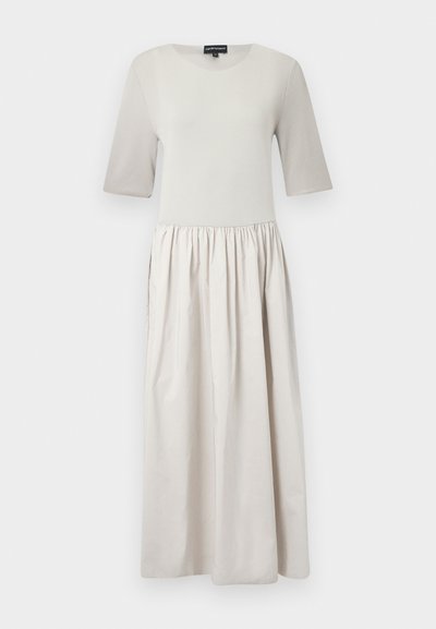 Šviesiai smėlio spalvos suknelė su prigludusia viršūne ir trumpomis rankovėmis, pereinanti į susiraukšlėjusią sijoną. Pagaminta iš minkštos medžiagos su lygia tekstūra.
