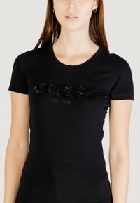 T-shirt in cotone nero con maniche corte, scollo rotondo, con la scritta "GUESS EST. 1981" in lettering nero testurizzato. Tessuto liscio.