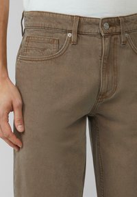 Pantalones de mezclilla marrón con un diseño de pierna recta, que cuentan con un cierre frontal de botón, estilo de cinco bolsillos y detalles de costura sutiles.