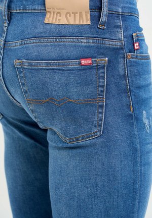 Mėlyni džinsai su liesu pjūviu, turintys lengvą nusidėvėjimą, kontrastingą siuvinėjimą ir dvi galines kišenes su prekės ženklo etiketėmis.