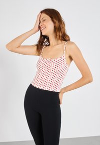 White tank top with red heart print, thin straps, and a small bow detail at the neckline, paired with black ribbed leggings.