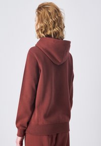 Hoodie couleur rouille en tissu doux. Comprend une capuche spacieuse, des manches longues et un ourlet côtelé pour le confort. Design épuré et minimal.