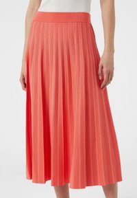 Koronkowa spódnica plisowana w kolorze koralowym z prążkowanym pasem; posiada pionowe białe paski. Miękka struktura tkaniny, fason w kształcie litery A, długość do kolan.