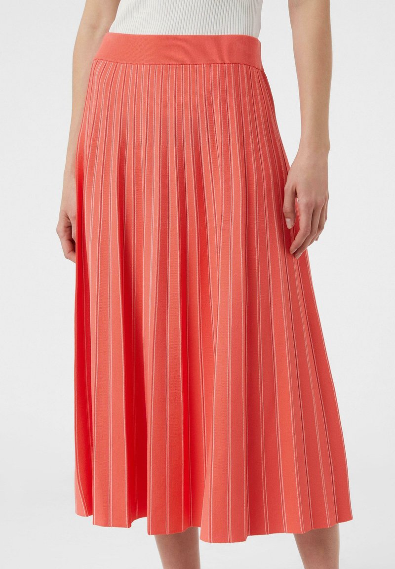Koronkowa spódnica plisowana w kolorze koralowym z prążkowanym pasem; posiada pionowe białe paski. Miękka struktura tkaniny, fason w kształcie litery A, długość do kolan.