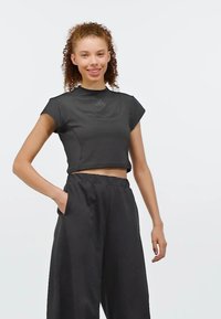 Svart kortärmad idrottstop med rund halsringning och subtil branding. Matchas med lösa svarta byxor med fickor.