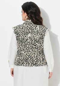 Leopardmönstrad denimväst med fransade fållar, ärmlös design och hög halsringning. Bärs över en ljusfärgad långärmad skjorta.