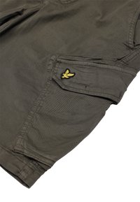 Pantaloni cargo verdi con una tasca a pattina visibile, con un logo giallo ricamato. Realizzati in tessuto resistente e strutturato con cuciture rinforzate.