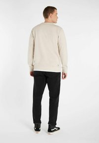 Crème-kleurige sweatshirt met lange mouwen, geribbelde manchetten en zoom, gecombineerd met zwarte broeken en zwarte sneakers met witte accenten.