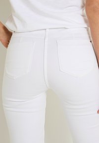 Jeans de mezclilla blanca con diseño ajustado, que cuentan con dos bolsillos traseros, detalles de costura y una textura lisa.