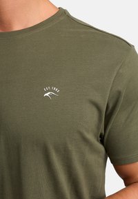 Olive green T-shirt made of soft cotton, featuring a crew neckline and short sleeves. White printed detail reading "EST. 1993" with a wave graphic.
