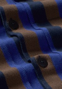 Wollen stof met horizontale strepen in blauw en bruin, voorzien van zwarte knopen. De textuur is geribbeld en tastbaar, wat diepte aan het ontwerp toevoegt.
