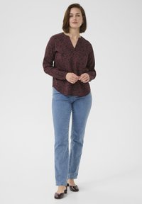 Bordeaux lange mouwen blouse met een bloemenpatroon, v-hals, gecombineerd met lichtblauwe jeans en donkere hakken.