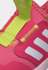 Κοντινή λήψη ροζ αθλητικού παπουτσιού με άσπρες ρίγες, φερμουάρ νέον κίτρινο και ραφές λεπτομέρειες.