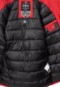 Interno di una giacca a vento nera imbottita con dettagli rossi, con un etichetta che riporta il logo del brand e un design intricato, e un piccolo connettore per cuffie.