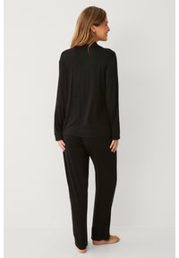 Ensemble composé d'un haut à manches longues noir et d'un pantalon, fabriqué en tissu doux. Présente une coupe décontractée et des coutures minimales pour le confort. Vue arrière affichée.