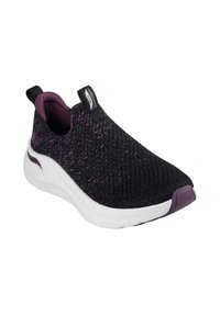 Zapatilla slip-on negra con parte superior de punto texturizado, acentos morados y suela blanca. Cuenta con un cuello acolchado y un diseño minimalista.