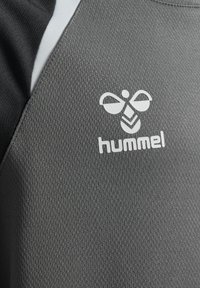Gros plan sur un tissu gris texturé avec un logo d'abeille stylisé blanc et le texte « hummel » imprimé sur le matériau.