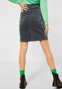 Jupe en denim grise avec des poches arrière et une fente. Associée à un haut vert et des bottines noires, avec des chaussettes vertes.