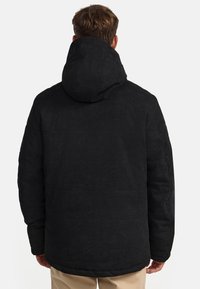 Jachetă puffer neagră dintr-un material texturat, având glugă și mansete elastice. Designul este oversized, cu un finisaj neted.